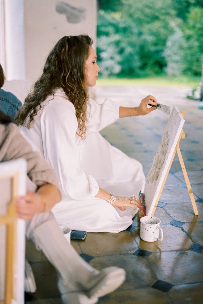 about-us-02 A woman artfully painting on canvas in a tranquil outdoor setting, embodying creativity and inspiration.